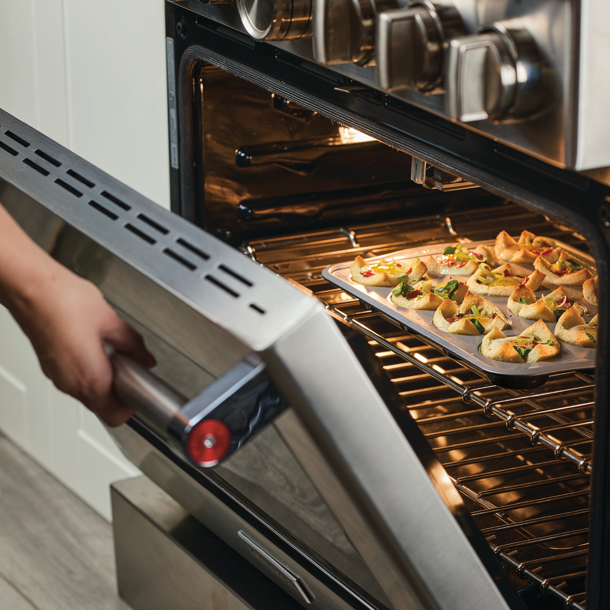 Person placing a tray of stuffed pastries into an oven.