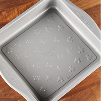 Square cake pan with a charming Mickey Mouse design on a wooden surface, ideal for your bakeware collection. Bake with the 9-Inch Nonstick Square Cake Pan and add a touch of magic to your creations!