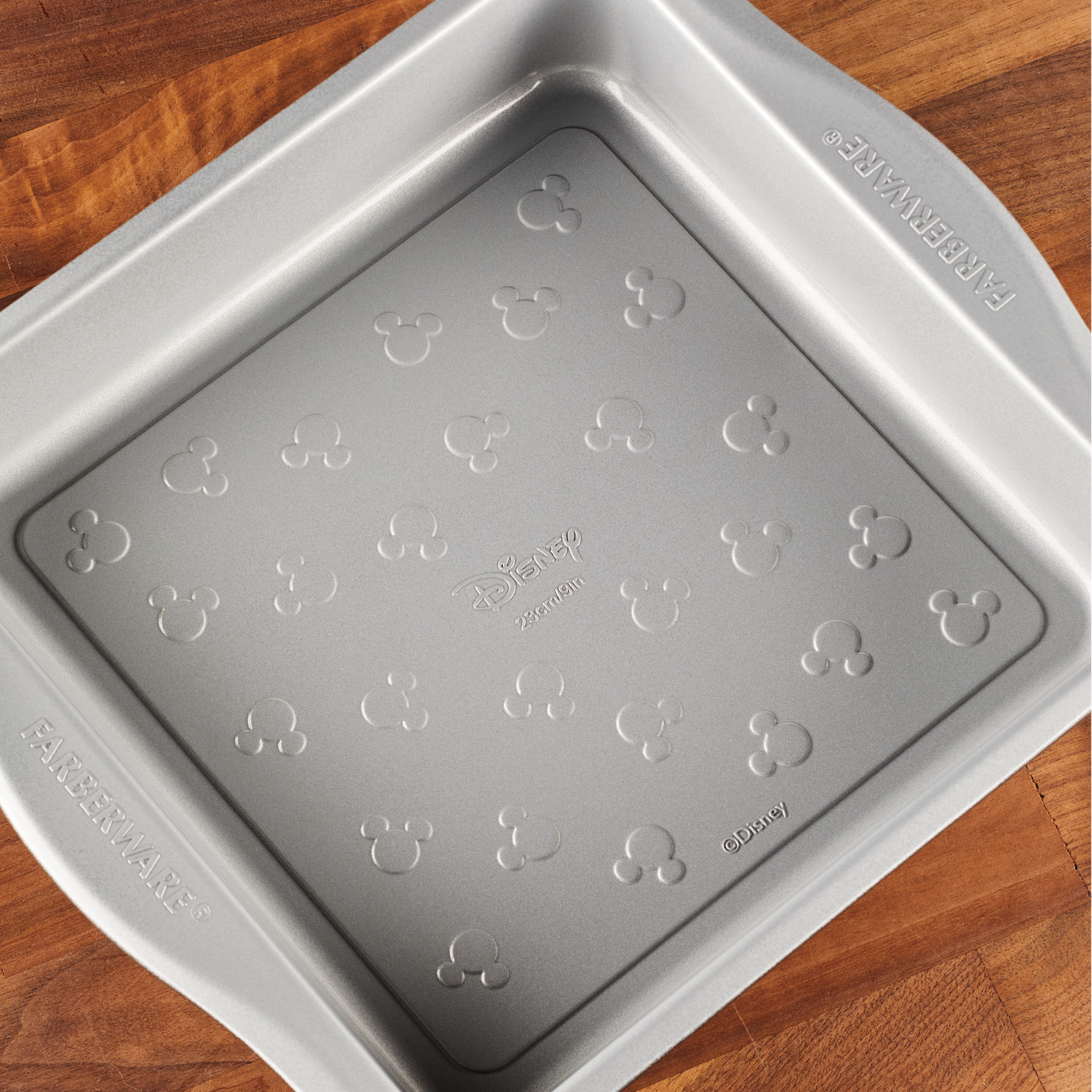 Square cake pan with a charming Mickey Mouse design on a wooden surface, ideal for your bakeware collection. Bake with the 9-Inch Nonstick Square Cake Pan and add a touch of magic to your creations!