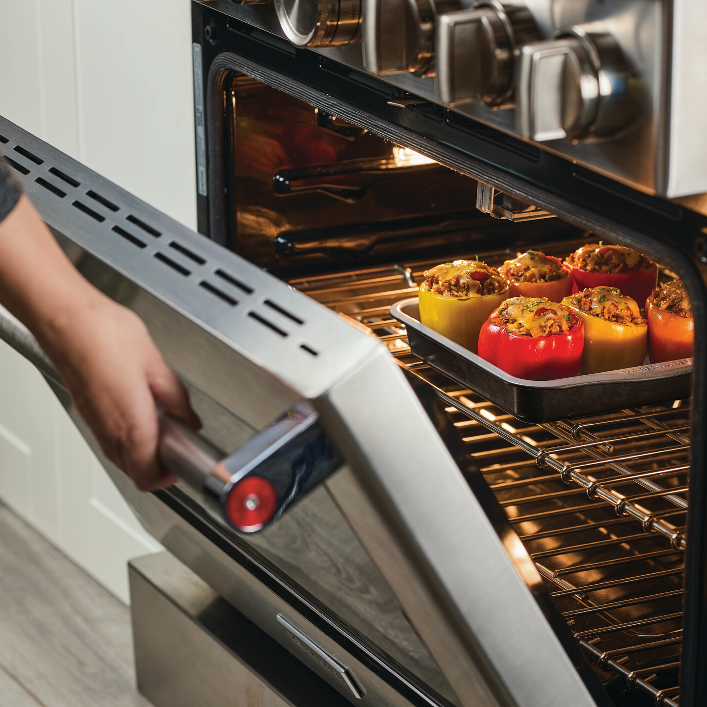 A person carefully places stuffed peppers into a preheated oven, using the vibrant 9-Inch Nonstick Square Cake Pan from the Bake with Mickey collection.