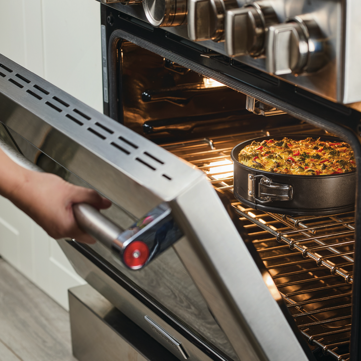 Person placing a casserole dish inside an open oven.