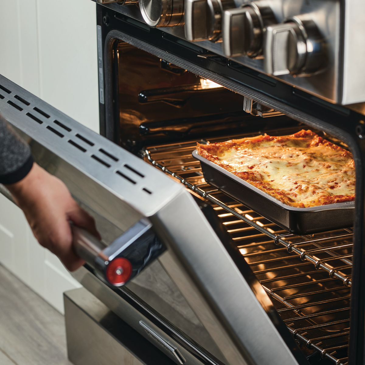 Person opening oven with lasagna baking inside.
