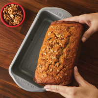Hands holding a freshly baked banana bread in a reliable 9"x5" Nonstick Loaf Pan next to a bowl of walnuts.