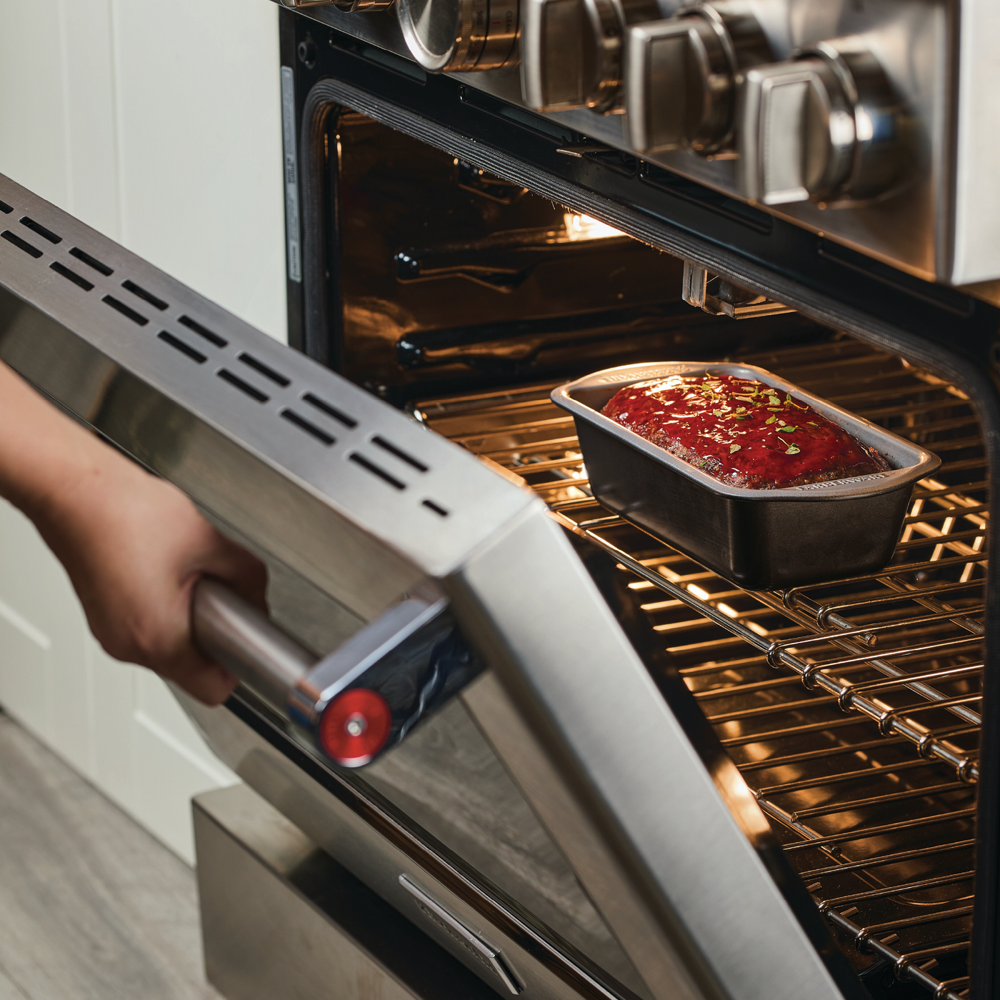 A person carefully places a loaf pan of savory meatloaf into the oven, using their favorite 9"x5" Nonstick Loaf Pan.