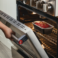 A person carefully places a loaf pan of savory meatloaf into the oven, using their favorite 9"x5" Nonstick Loaf Pan.