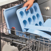 Blue baking trays being placed in a dishwasher.