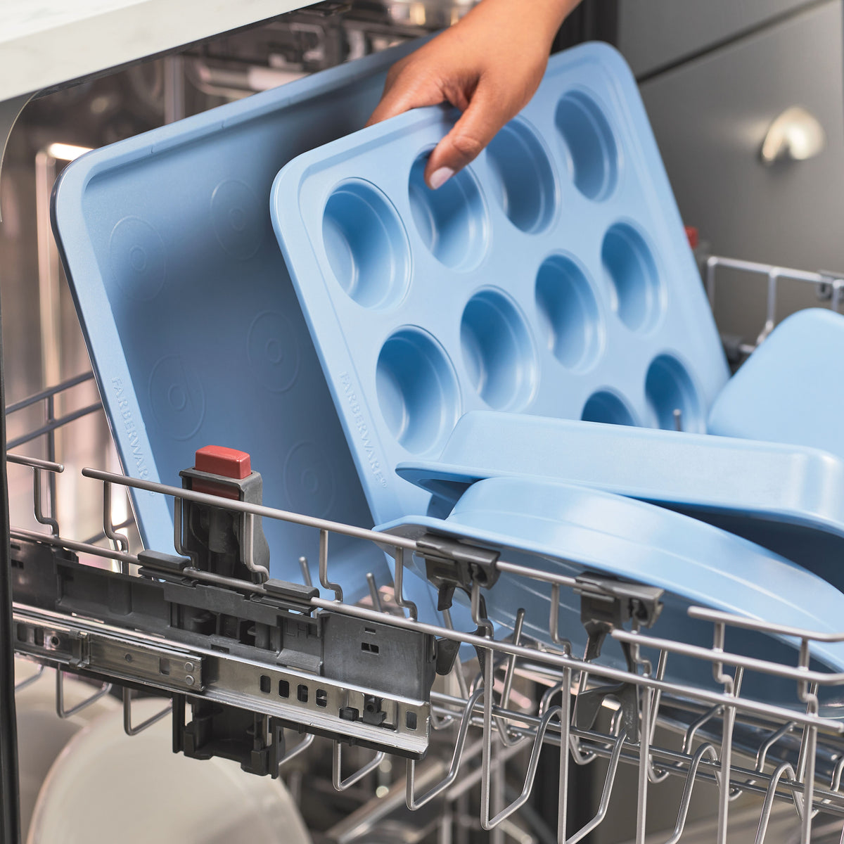 Blue baking trays being placed in a dishwasher.