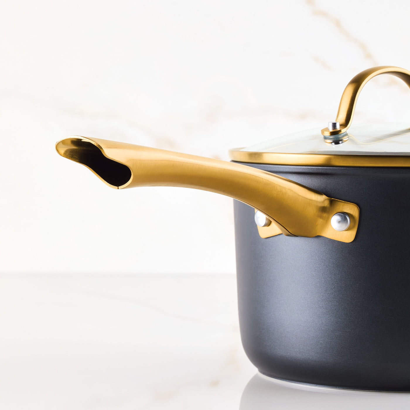 Cookware set with gold handle and lid on a marble surface.