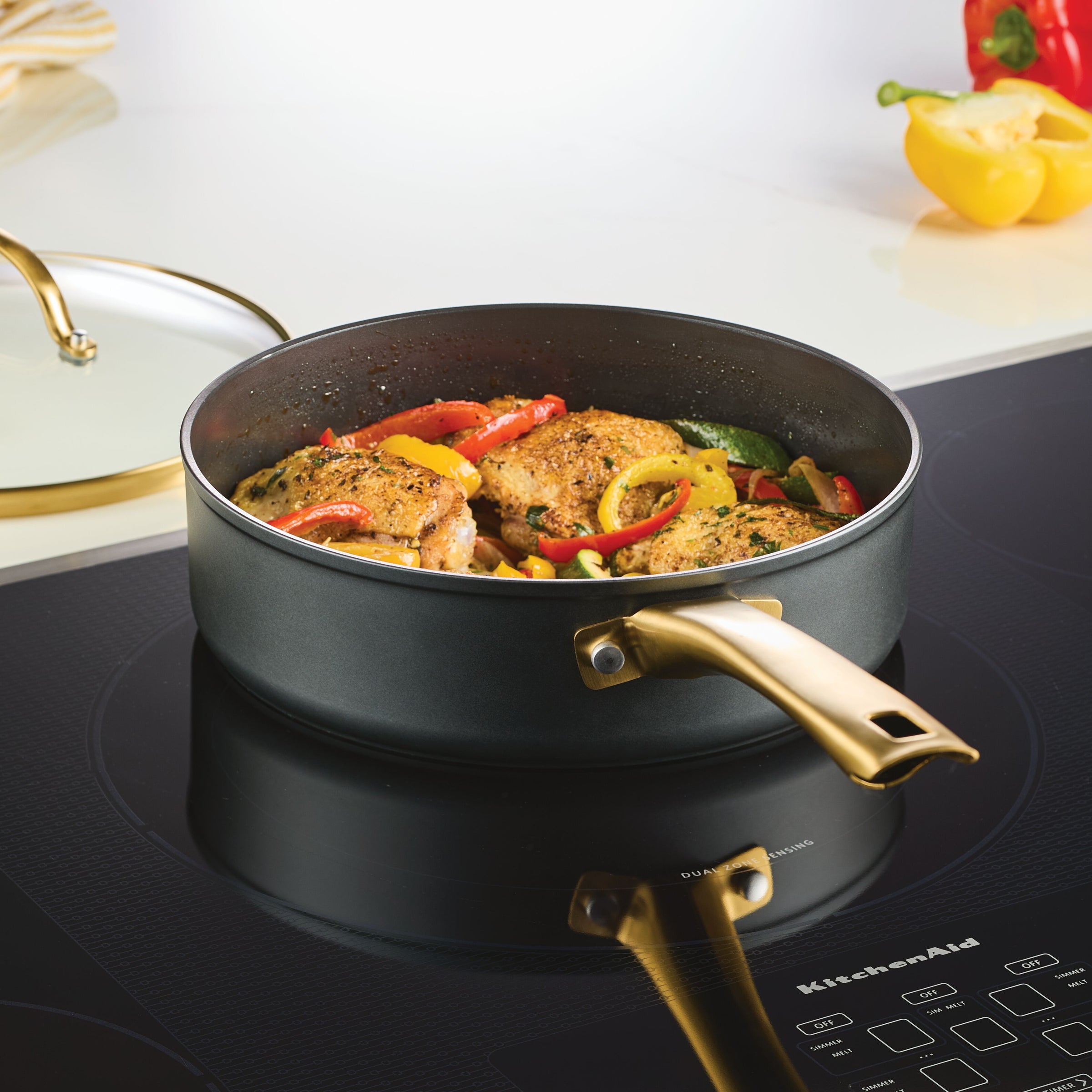 Part of the Forged Induction Ceramic 12-Piece Cookware Set, a frying pan with cooked chicken and vegetables sits on the stovetop, ready to serve a delicious meal.