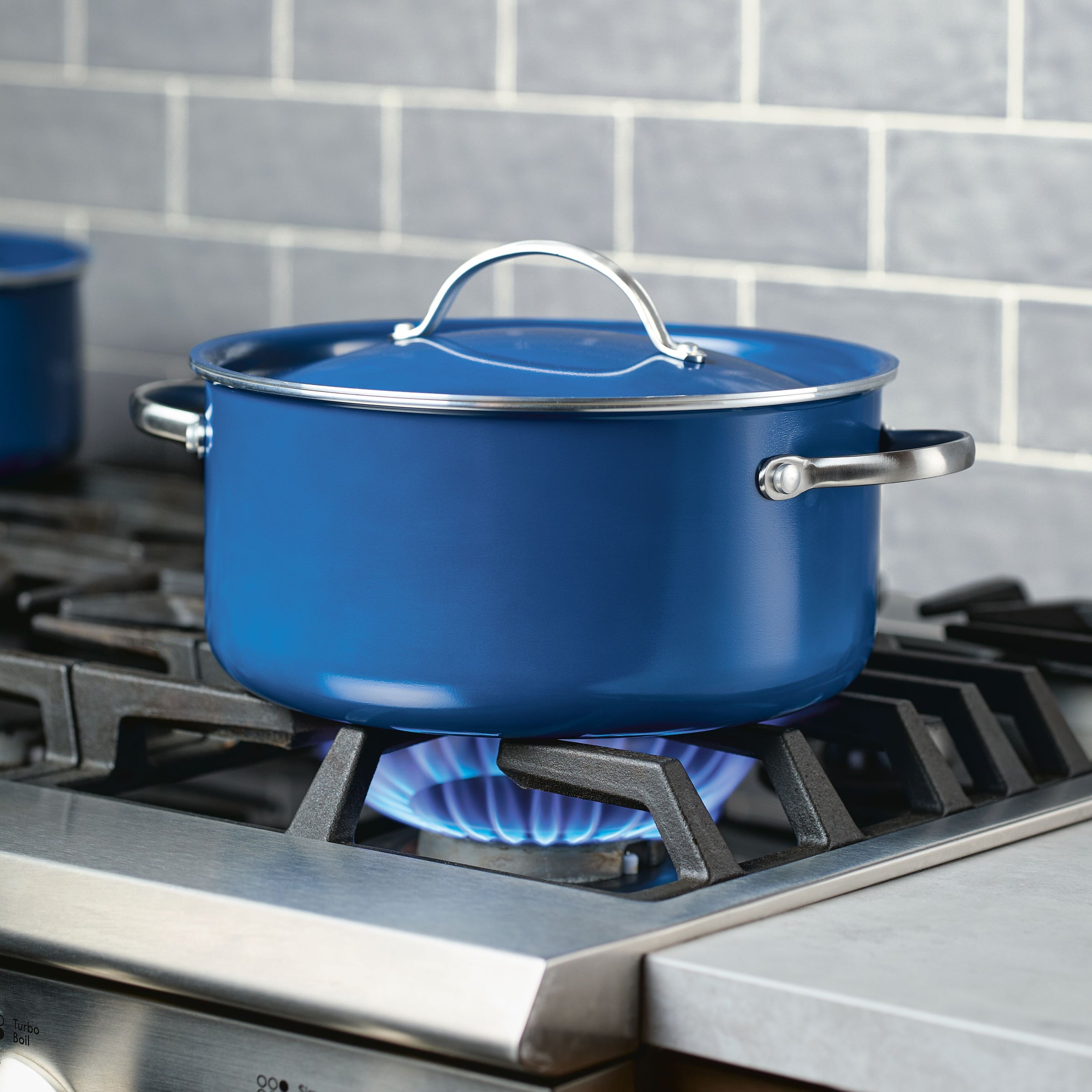 A beautifully crafted pot from the 12 Piece Ceramic Nonstick Cookware Set sits on the gas stove with a lit burner, highlighting its dishwasher-safe attributes.
