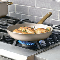 Chicken breasts sizzle in a frying pan on the stovetop, ensuring even heat distribution. The Radiant Nonstick 12-Piece Cookware Set features a sleek gold accent handle, adding a touch of elegance to your cooking experience.