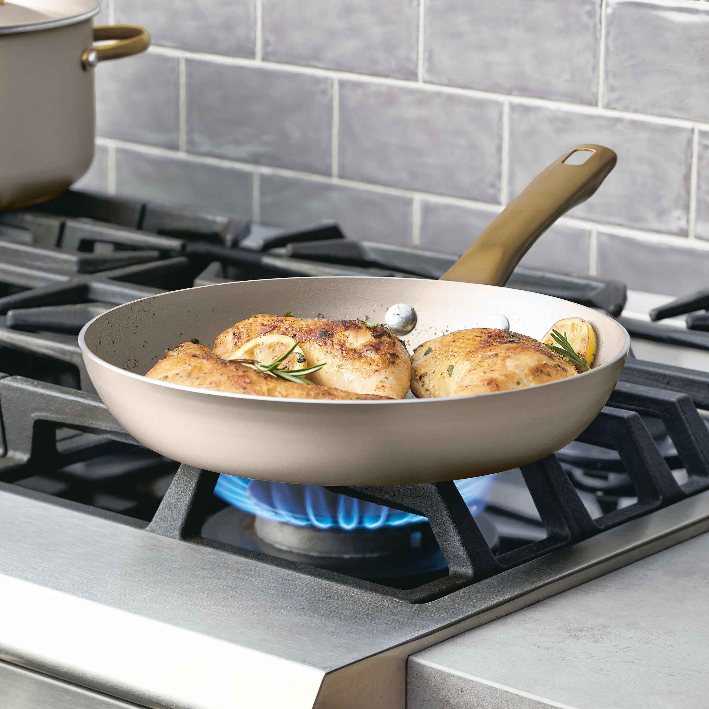 Chicken breasts sizzle in a frying pan on the stovetop, ensuring even heat distribution. The Radiant Nonstick 12-Piece Cookware Set features a sleek gold accent handle, adding a touch of elegance to your cooking experience.