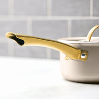 A saucepan from the Radiant Nonstick 12-Piece Cookware Set, known for its even heat distribution, sits on a light gray countertop with a tiled background.