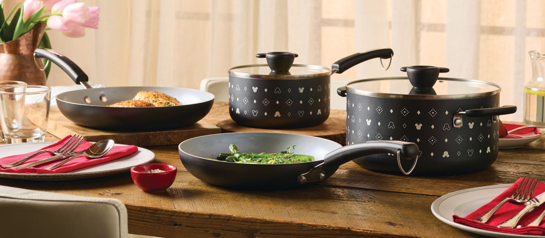 A set of black cookware with dishes on a wooden dining table.