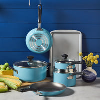 A 15-Piece Nonstick Cookware Set in teal, made from heavy gauge aluminum, is complemented by corn, Brussels sprouts, and decor on a counter.