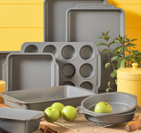 The 10-Piece Nonstick Bakeware Set in gray is elegantly displayed on the kitchen counter, complemented by fresh green apples.