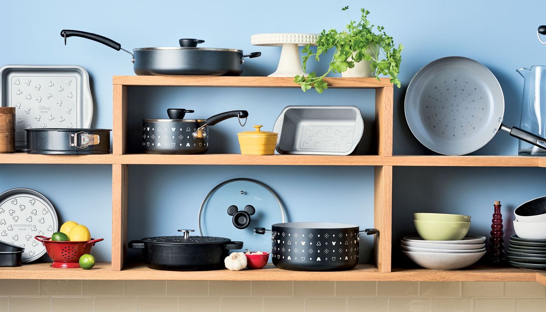 Farberware Disney cookware on wooden open shelving. It features a black and white aesthetic with Mickey Mouse silhouettes and diamond patterns on the cookware and bakeware.