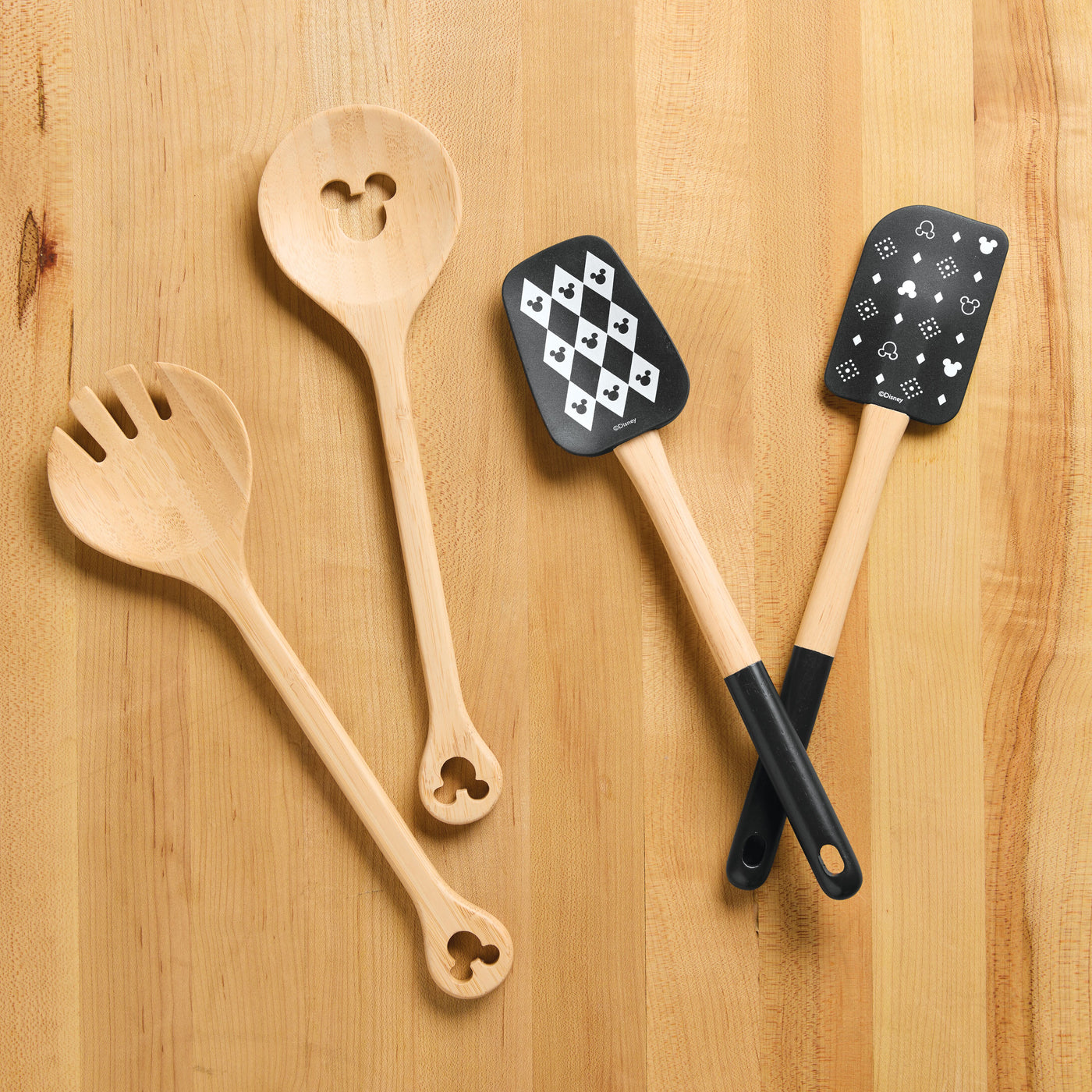 The Monochrome Kitchen Tool Set, featuring four utensils with themed cutouts and prints, elegantly rests on a wooden surface, adding a whimsical Disney touch to your culinary space.