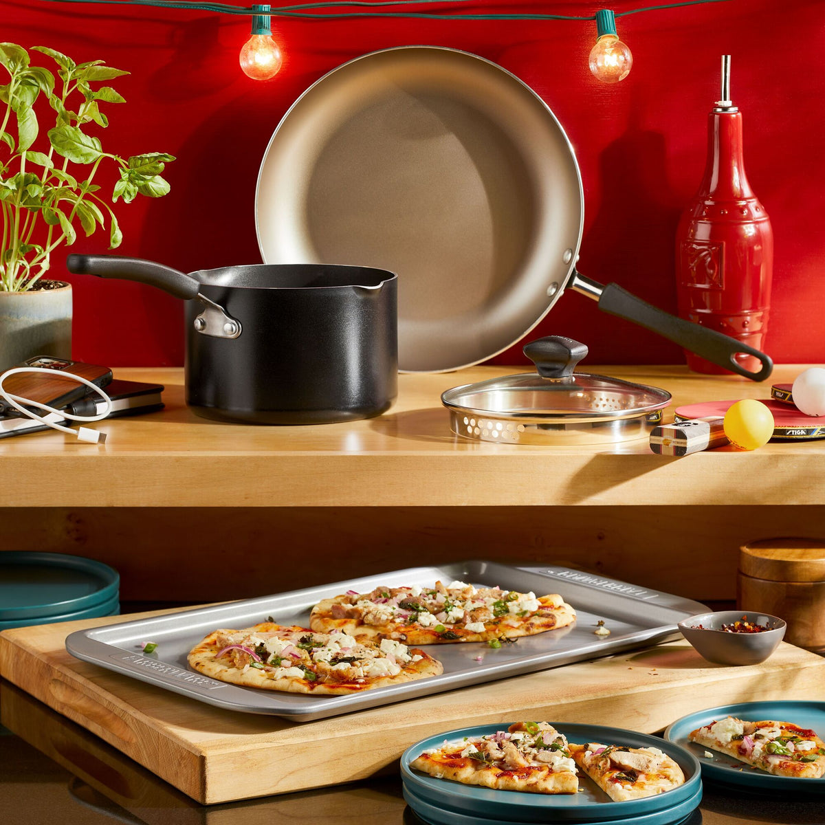 Kitchen counter with cookware, pizza on tray, and string lights.