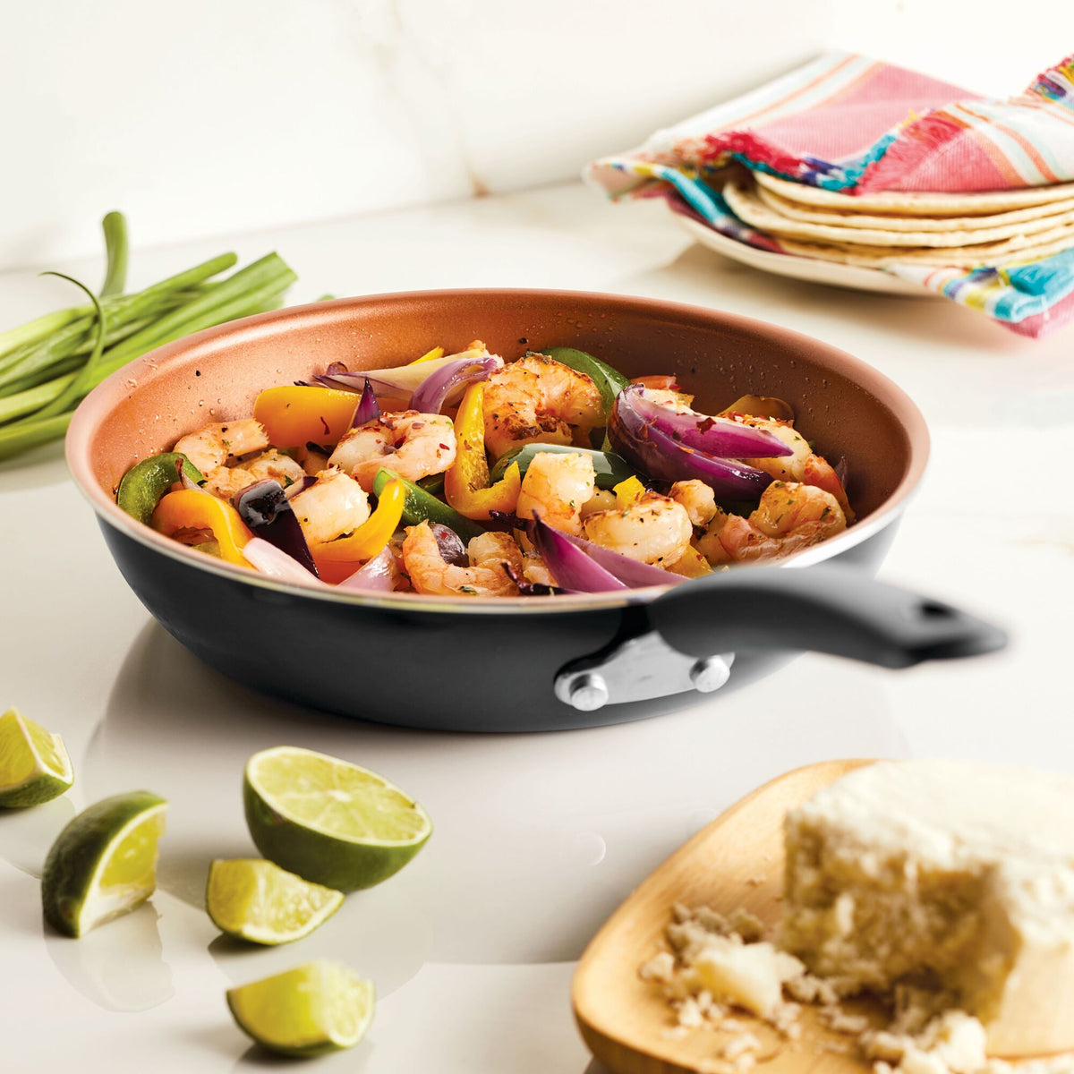 A skillet with shrimp and mixed vegetables next to limes and cheese.