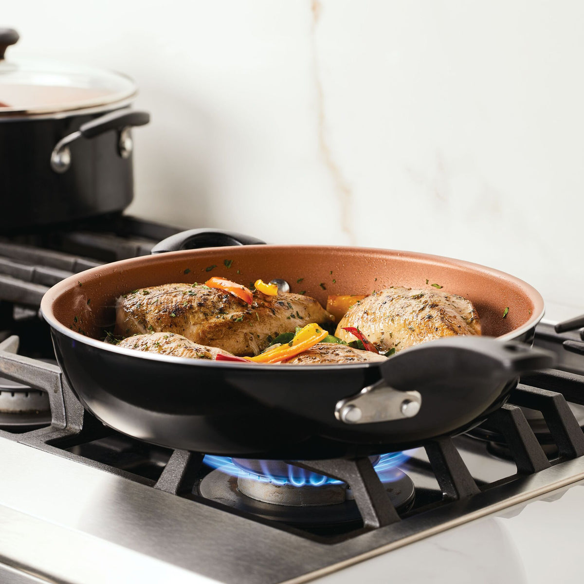 Chicken and vegetables cooking in a skillet on a gas stove.