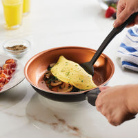 Person cooking an omelette with mushrooms and herbs in a non-stick pan.