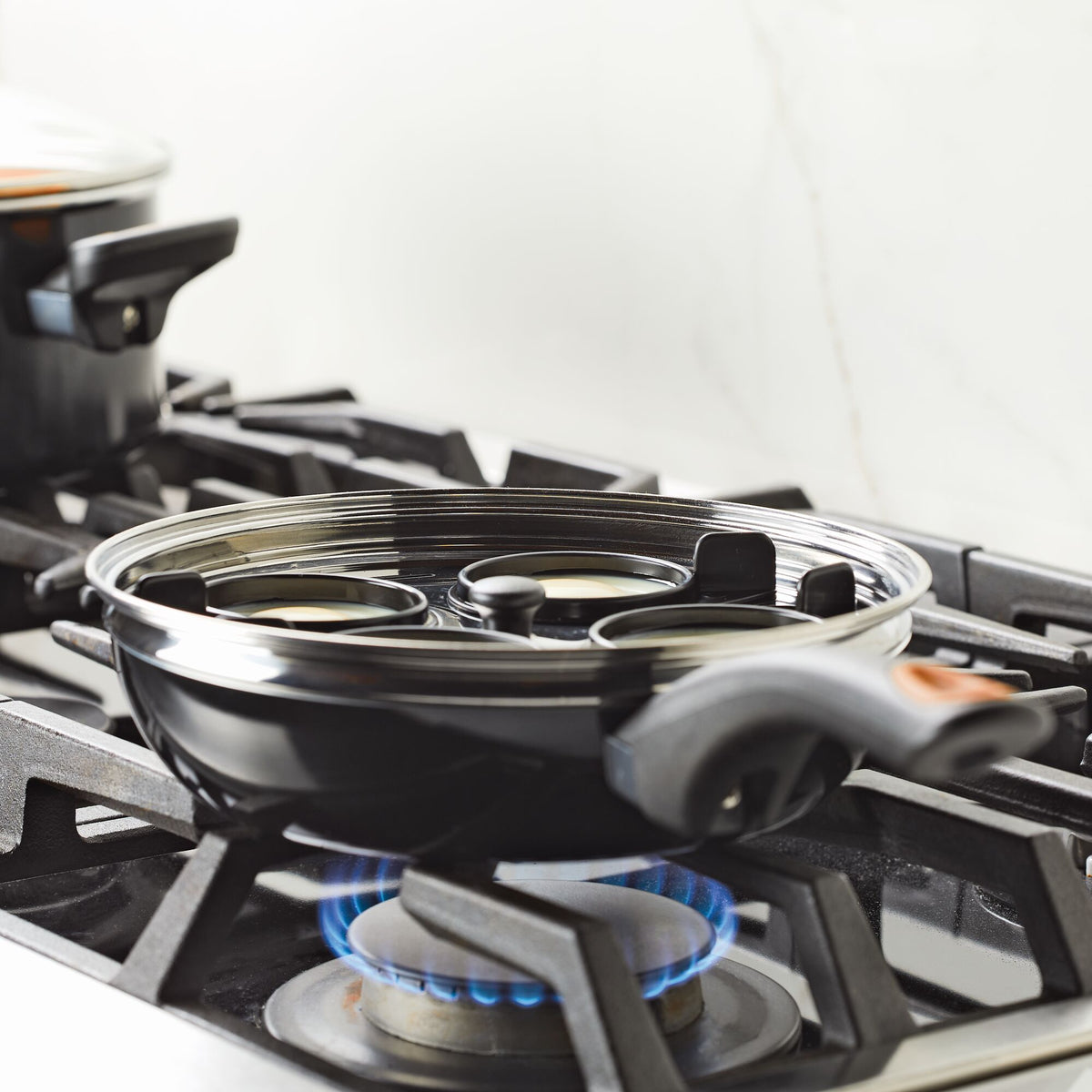 Frying pan on gas stove with four round sections and visible blue flame.