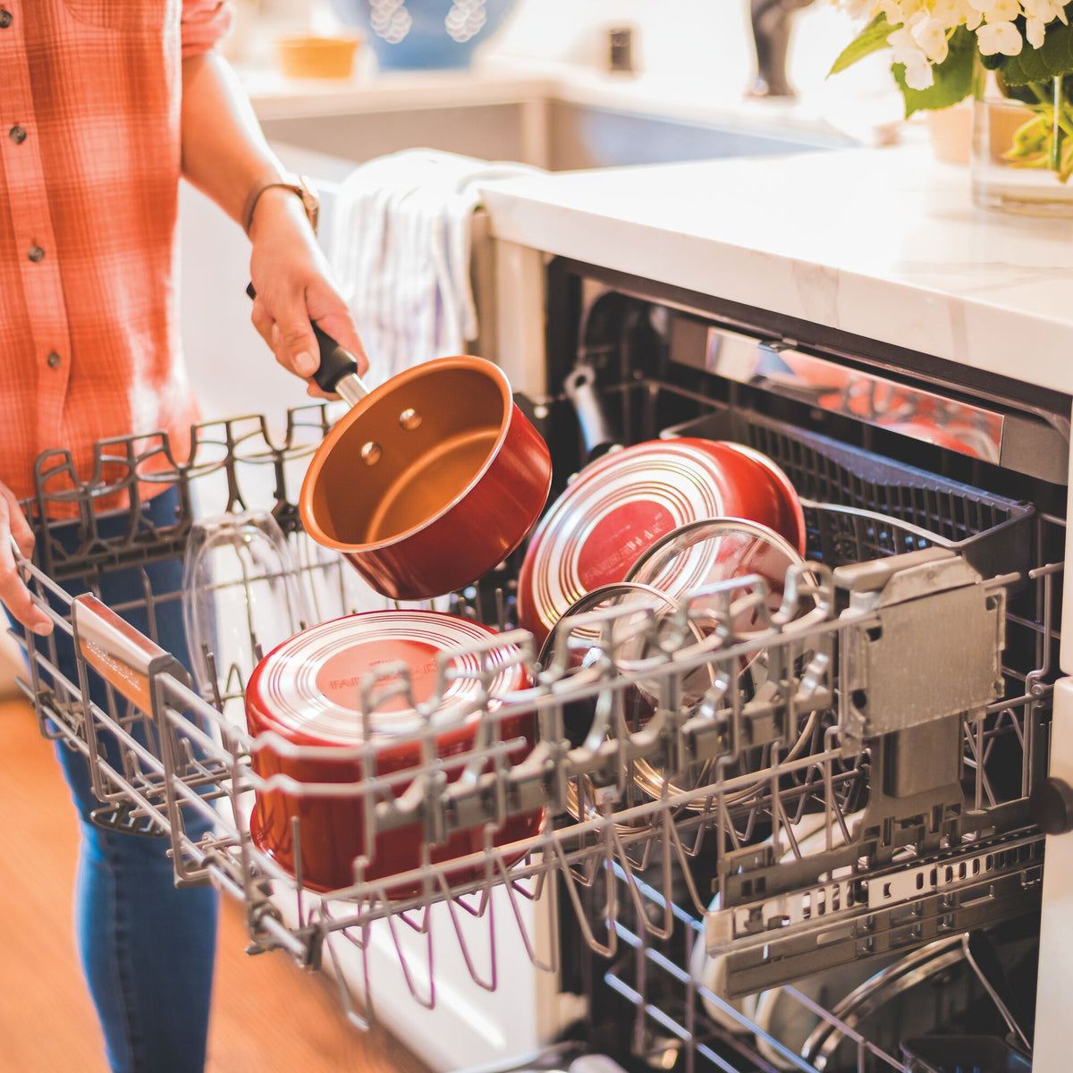 Person loading red pots into a dishwasher.