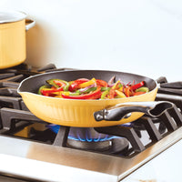 Yellow frying pan on stove with sliced vegetables being sautéed.