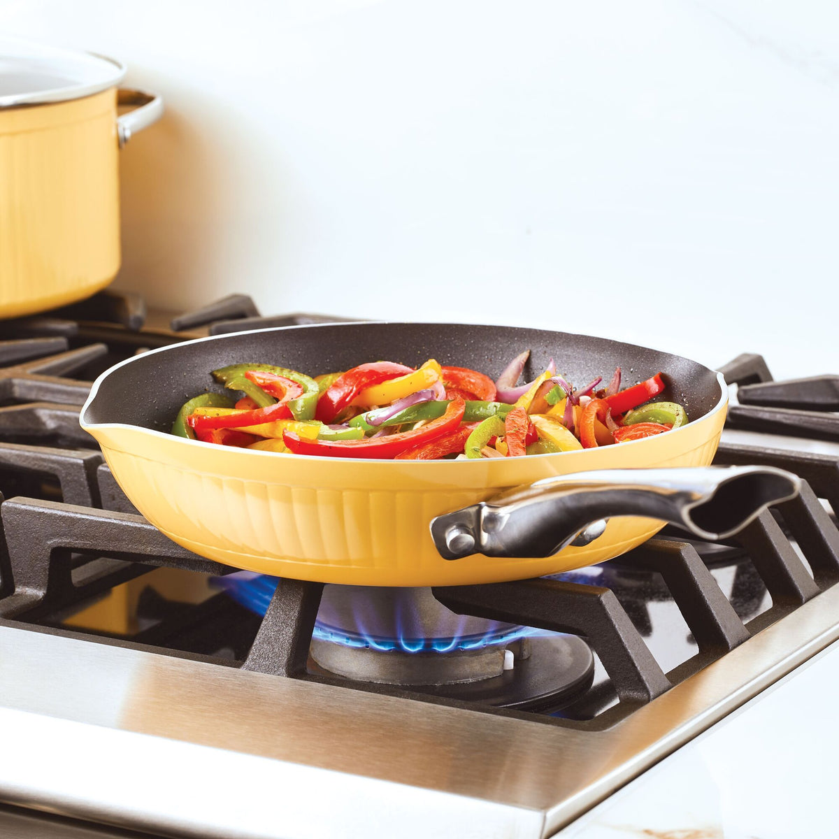 Yellow frying pan on stove with sliced vegetables being sautéed.