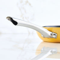 Close-up of a yellow pan with a shiny metal handle on a white surface.