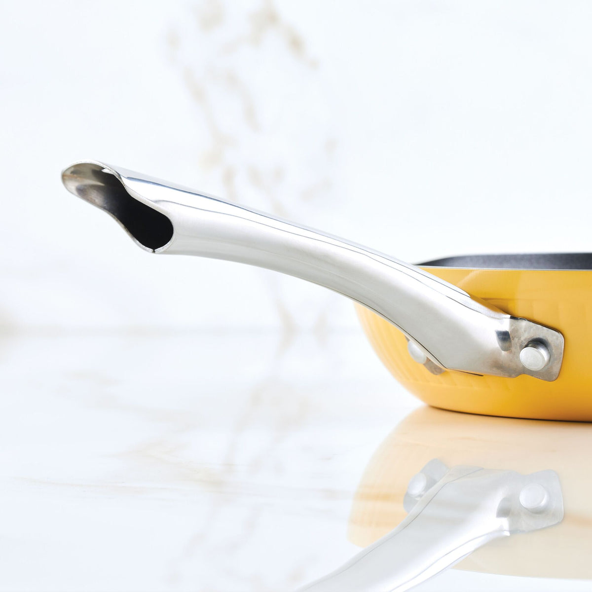 Close-up of a yellow pan with a shiny metal handle on a white surface.