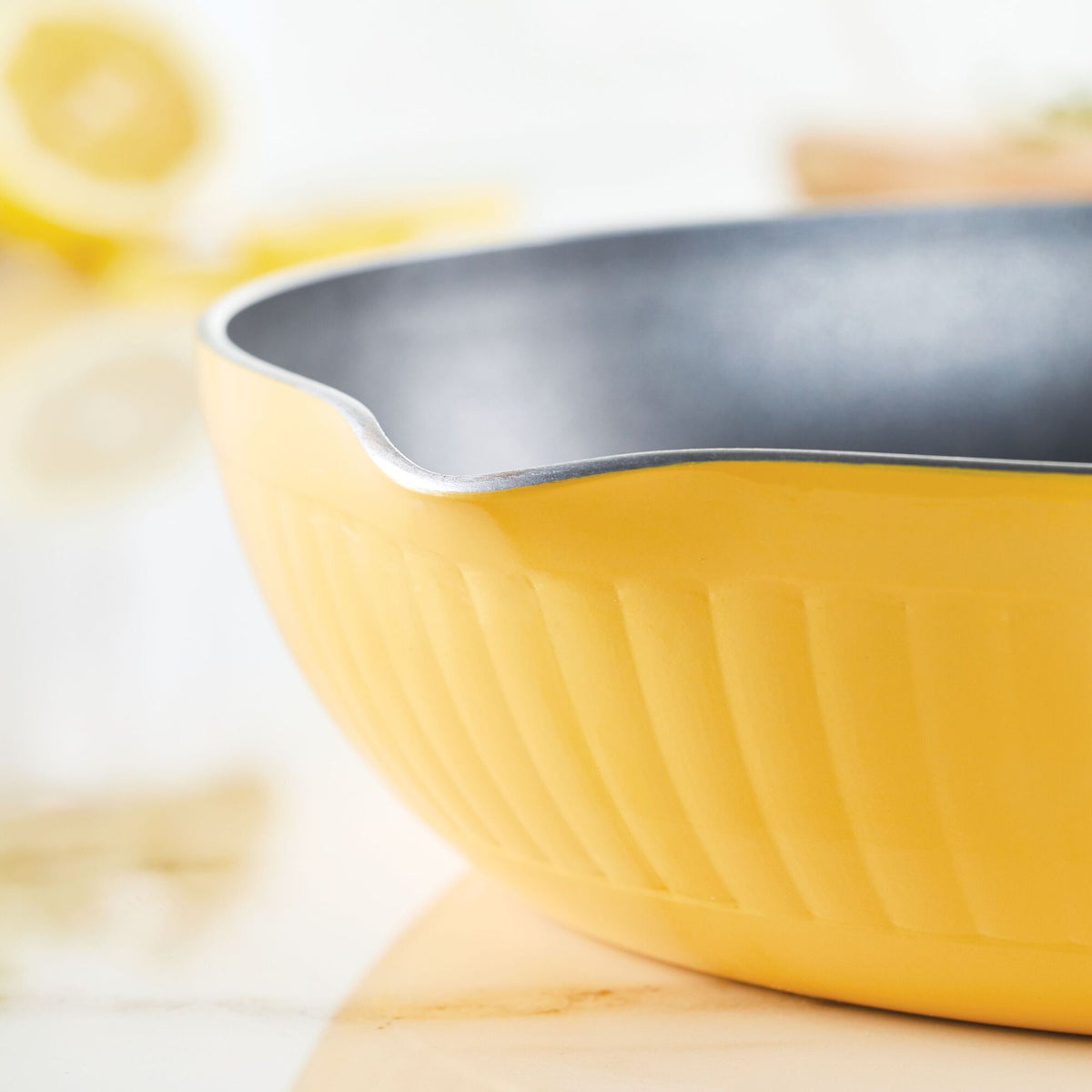 Close-up of a yellow mixing bowl with a spout on a light surface.