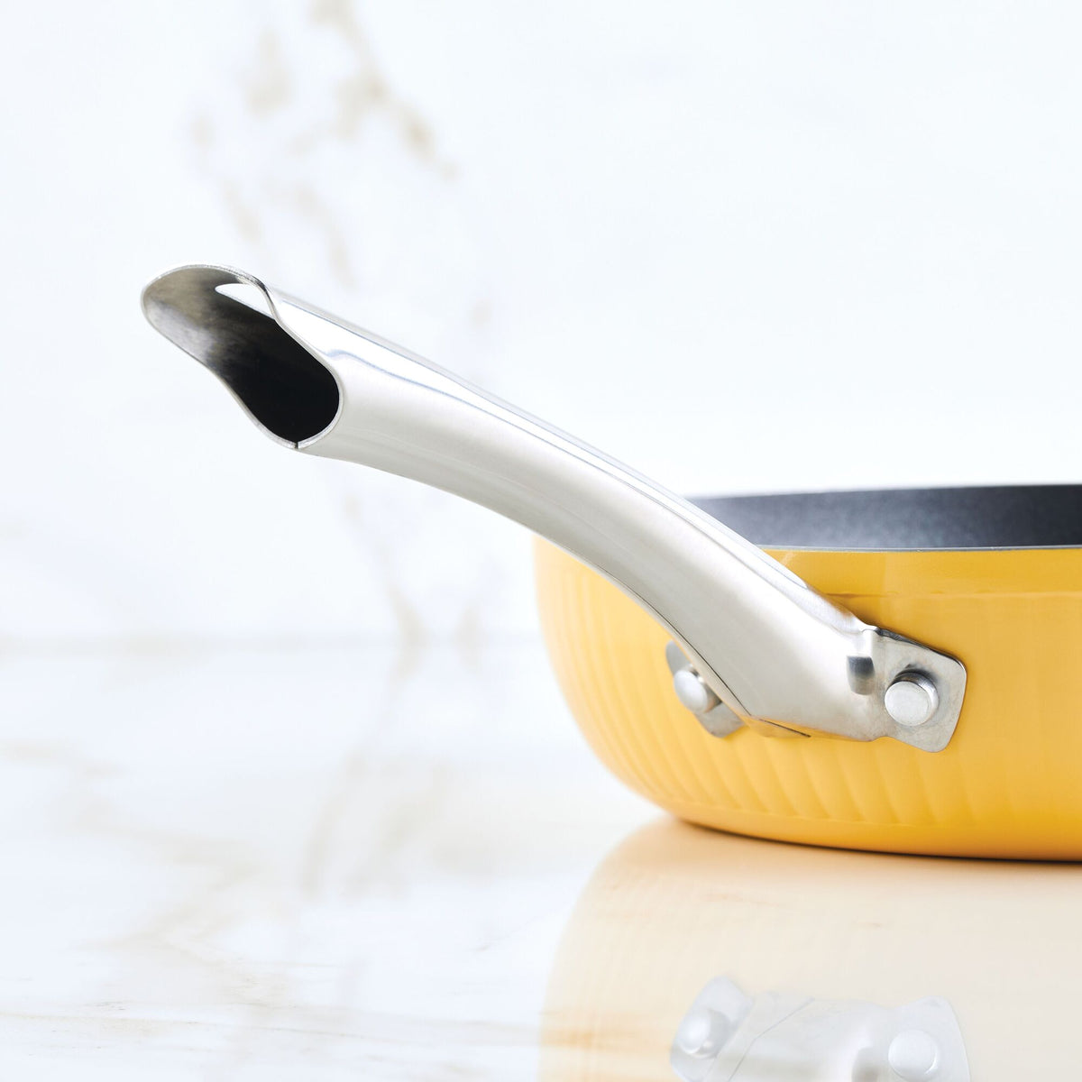 Yellow frying pan with a silver handle on a marble surface.