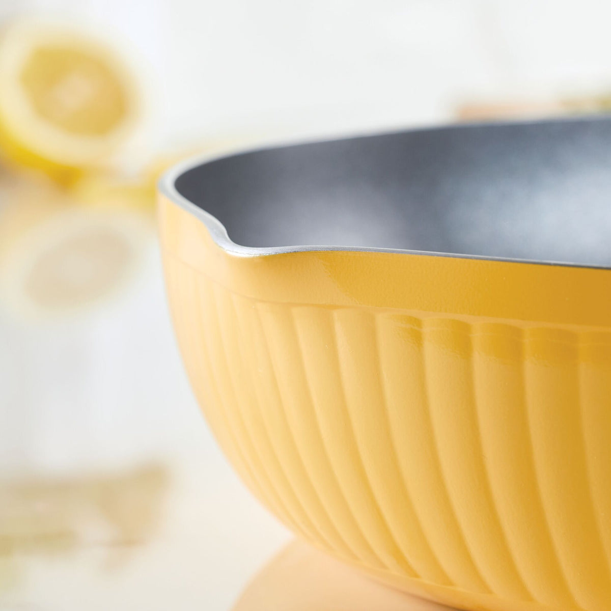 Close-up of a yellow mixing bowl with a pouring spout on a reflective surface.