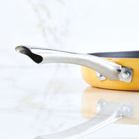 Yellow frying pan with a stainless steel handle on a marble countertop.