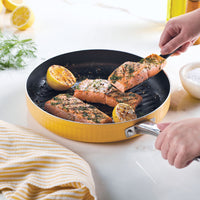 Hands cooking seasoned salmon and lemon halves in a yellow frying pan.