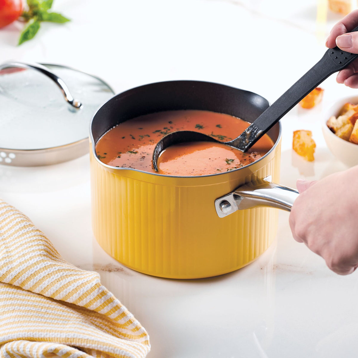 Person ladling soup from a yellow pot on a kitchen counter.