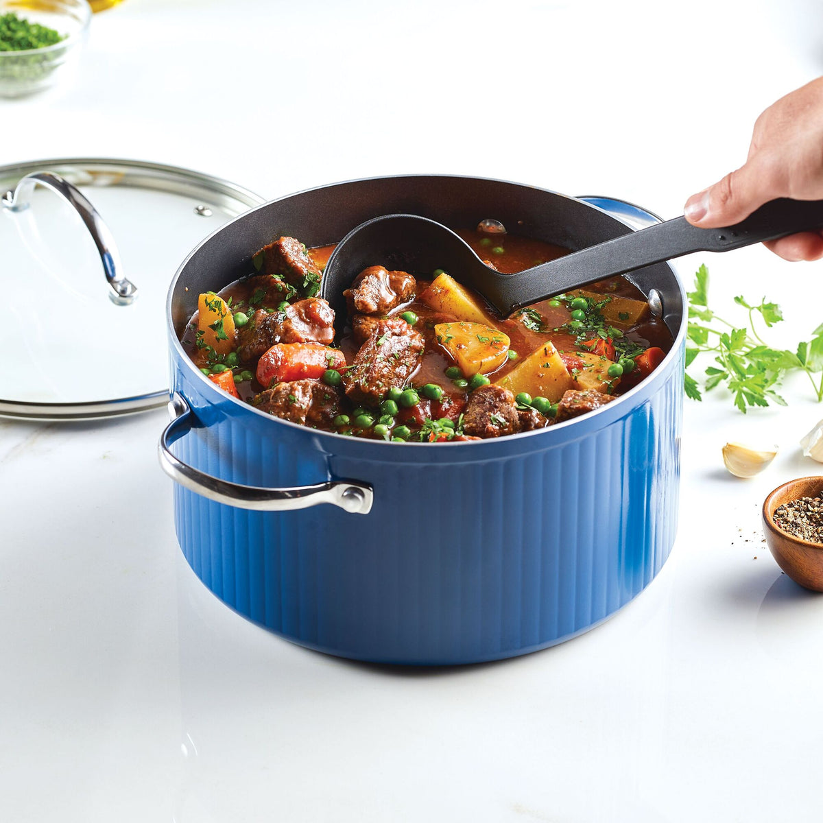 Hand ladling stew from a blue pot on a kitchen counter.