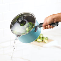 Hand holding pot with lid, draining water from cooked vegetables.