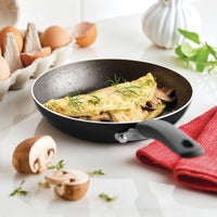 Omelet with herbs and mushrooms in a frying pan on a white countertop.