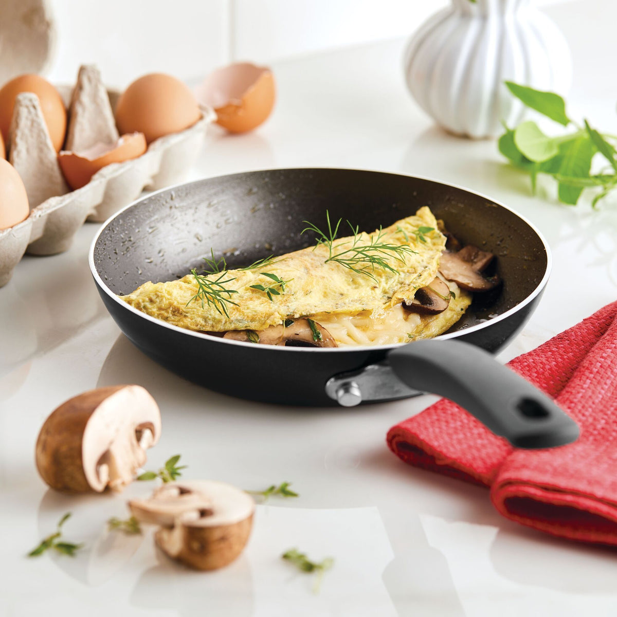 Omelet with herbs and mushrooms in a frying pan on a white countertop.