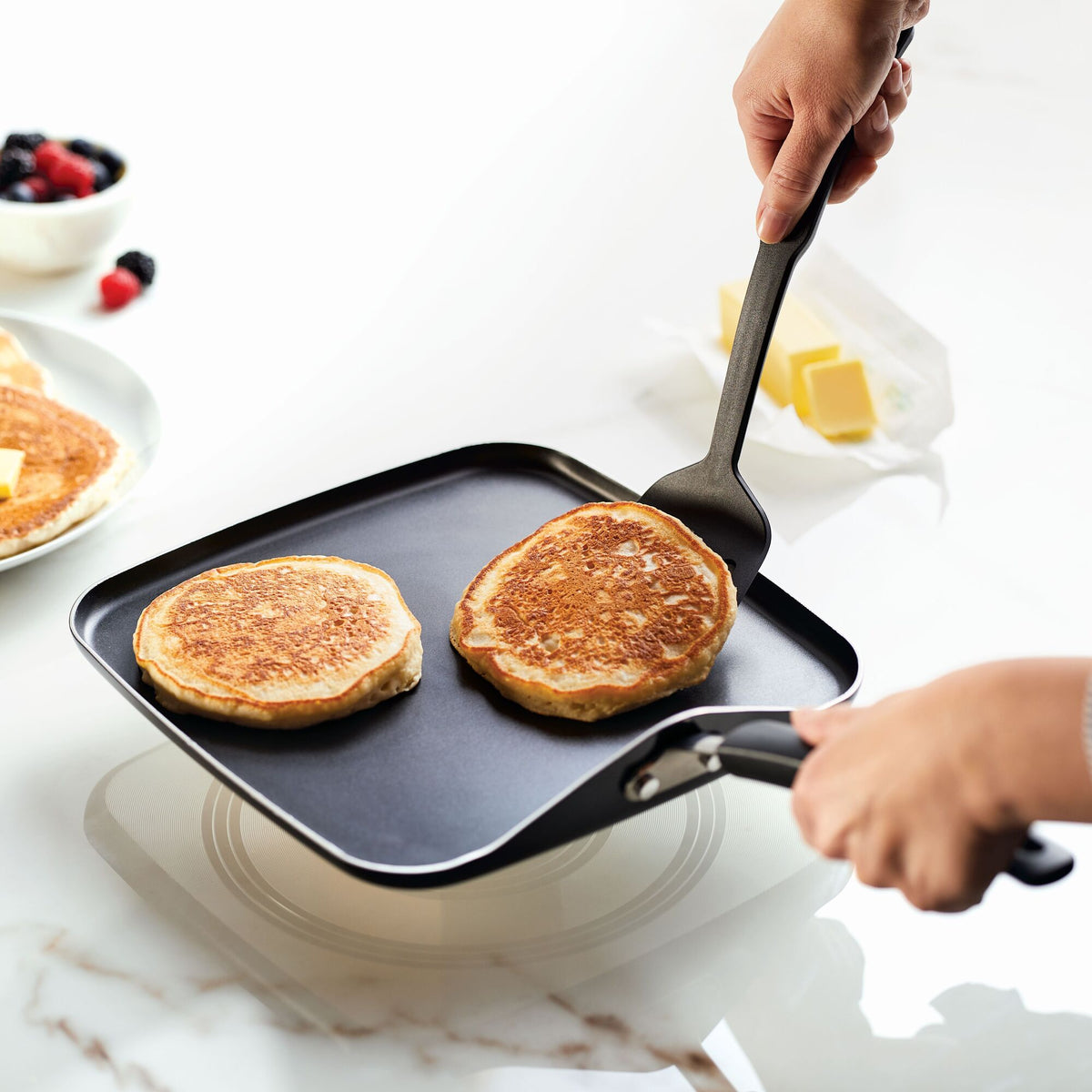Person flipping pancakes on a griddle with a spatula.