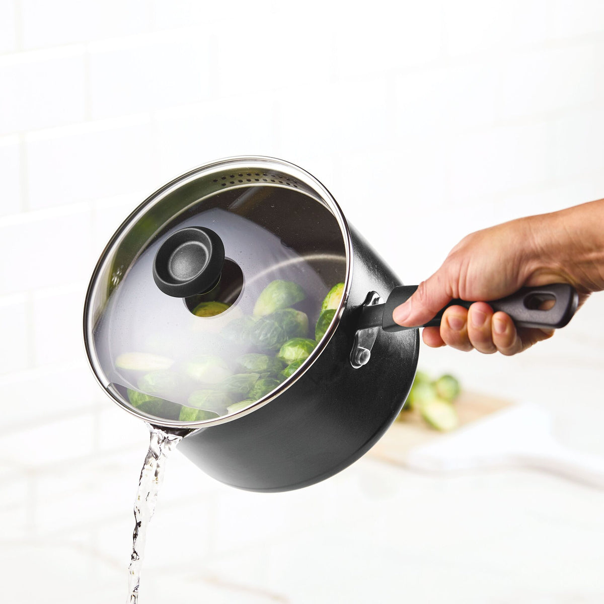 Hand pouring water from a pot with a lid, Brussels sprouts inside.