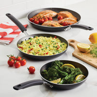 Three frying pans with salmon, rice, and broccoli on a kitchen counter.