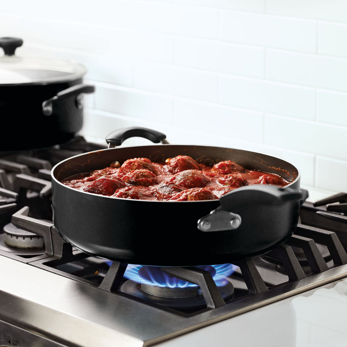 Meatballs in tomato sauce simmering in a pan on a gas stove.