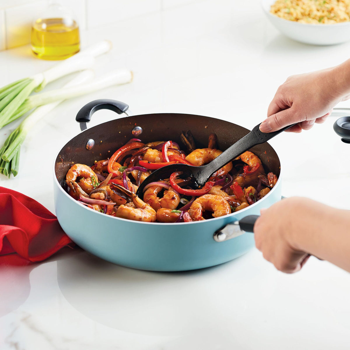 A person stir-frying shrimp and vegetables in a blue pan on a stovetop.