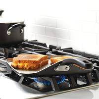 Two grilled cheese sandwiches cooking on a stovetop griddle.