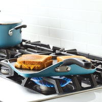 Grilled cheese sandwiches cooking on a griddle over a gas flame on the stove.