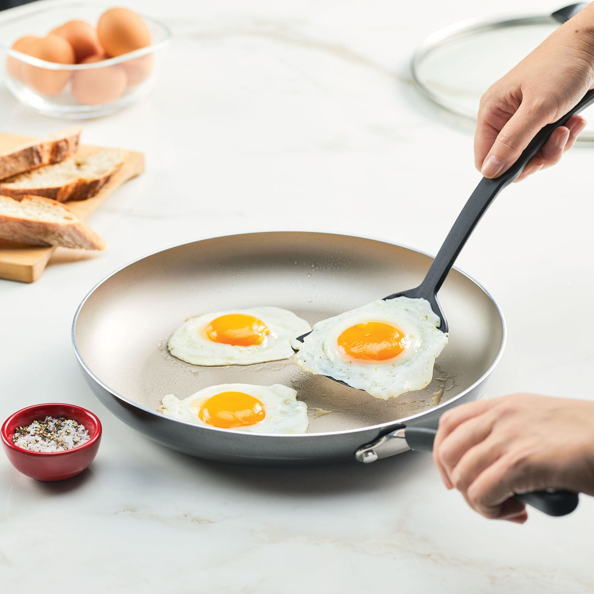 Person cooking three sunny-side-up eggs in a frying pan.